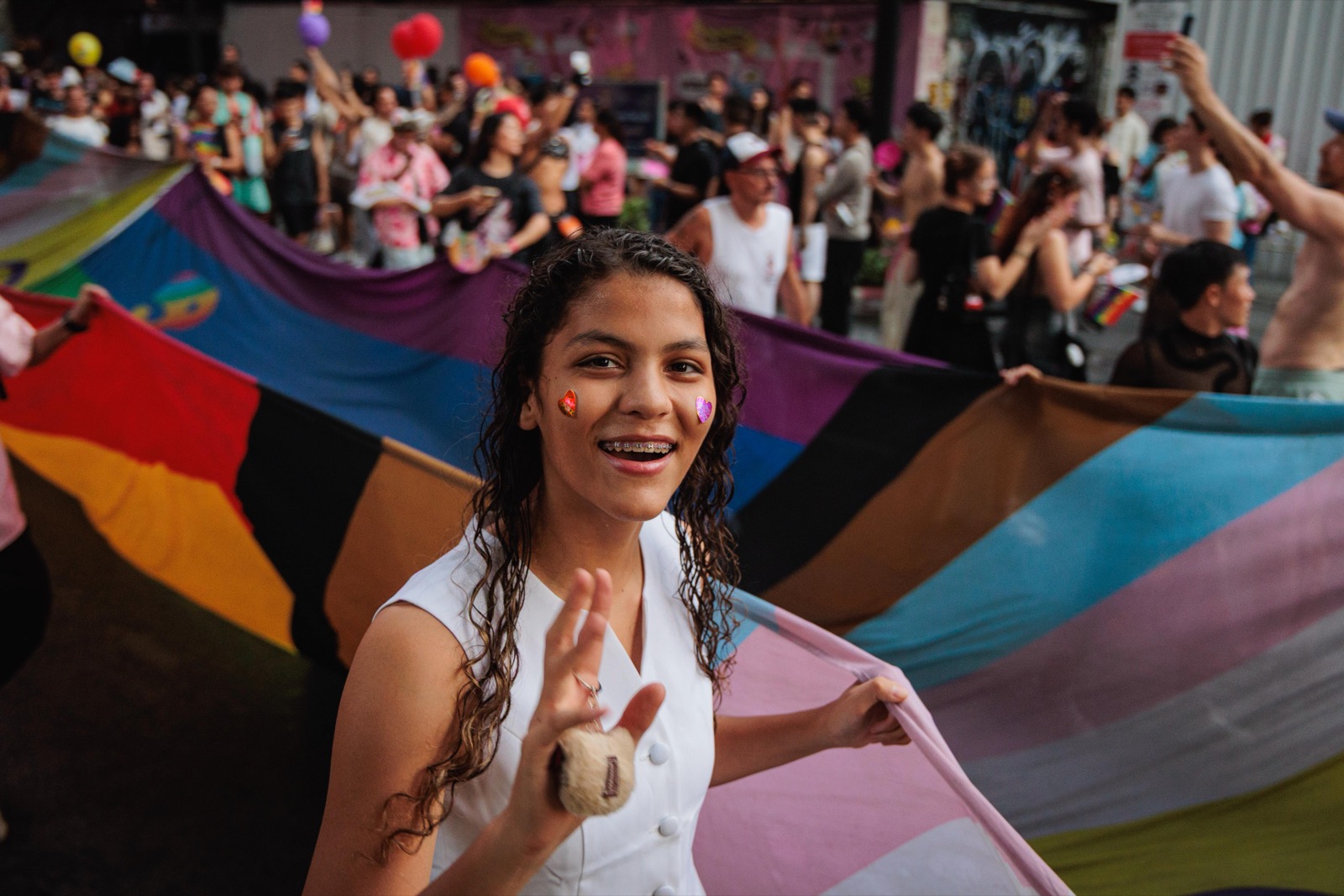 A smiling young woman at a Pride march, holding a Pride flag with the crowd behind her
